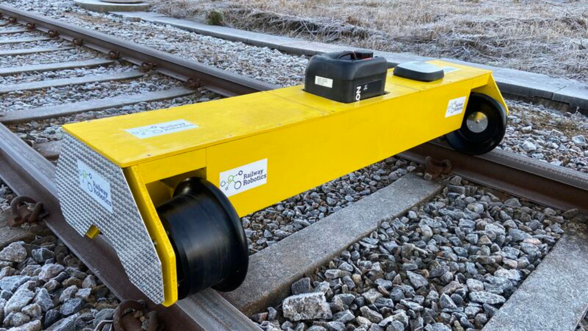 Compact yellow automated track inspection robot positioned on railway rails during testing.