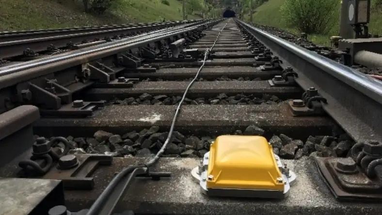Yellow trackside sensor device mounted between railway tracks with a cable running along the ballast